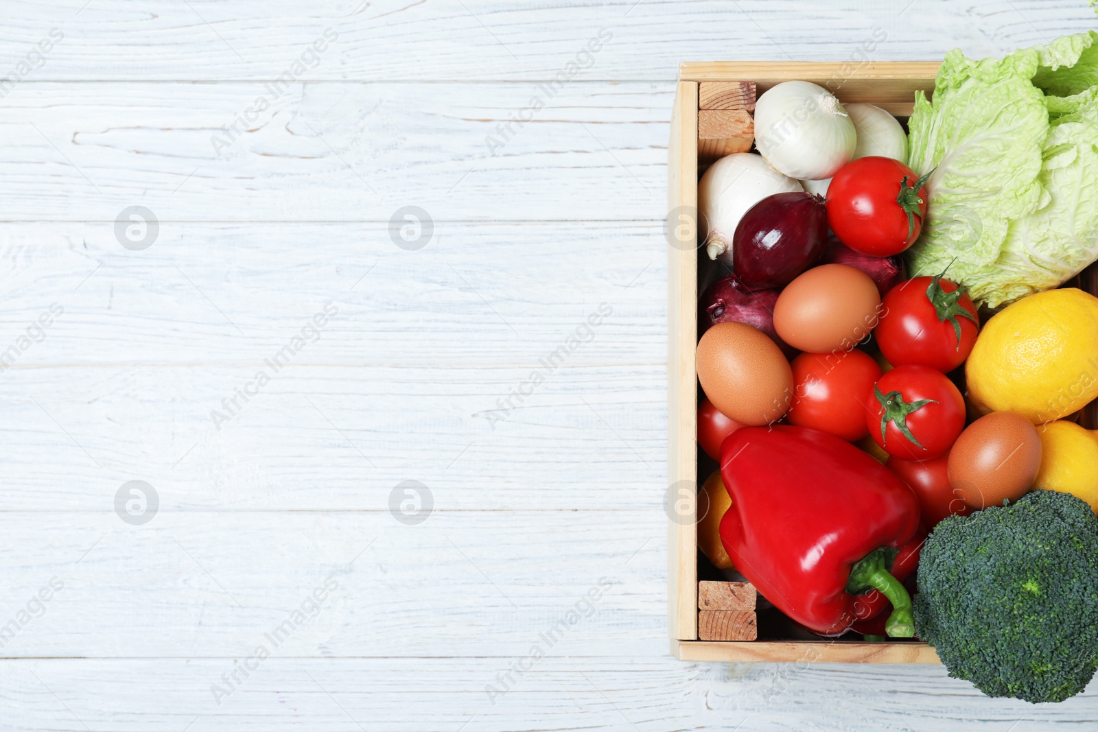 Photo of Wooden crate full of fresh products on light background, top view. Space for text