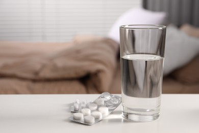 Glass of water and different pills in blisters on white table indoors, space for text