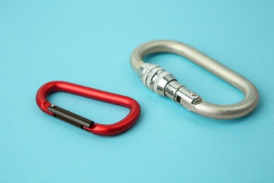 Photo of Two metal carabiners on light blue background, closeup