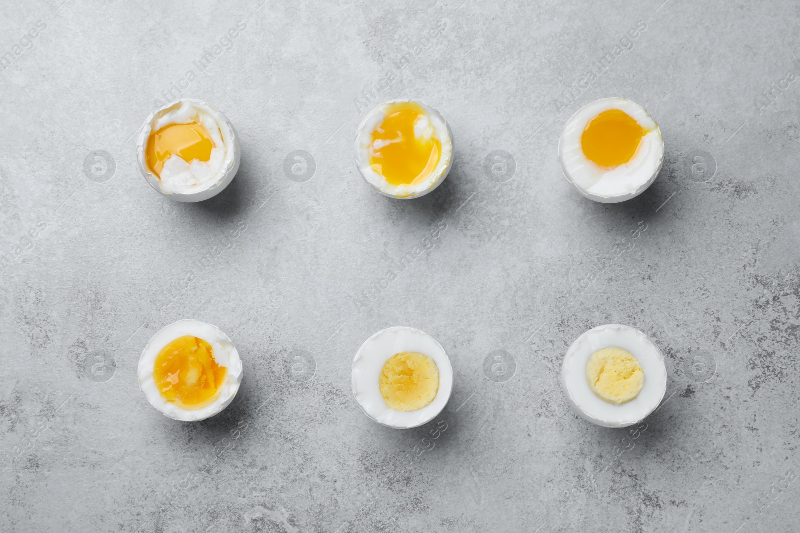 Photo of Different readiness stages of boiled chicken eggs on light grey table, flat lay