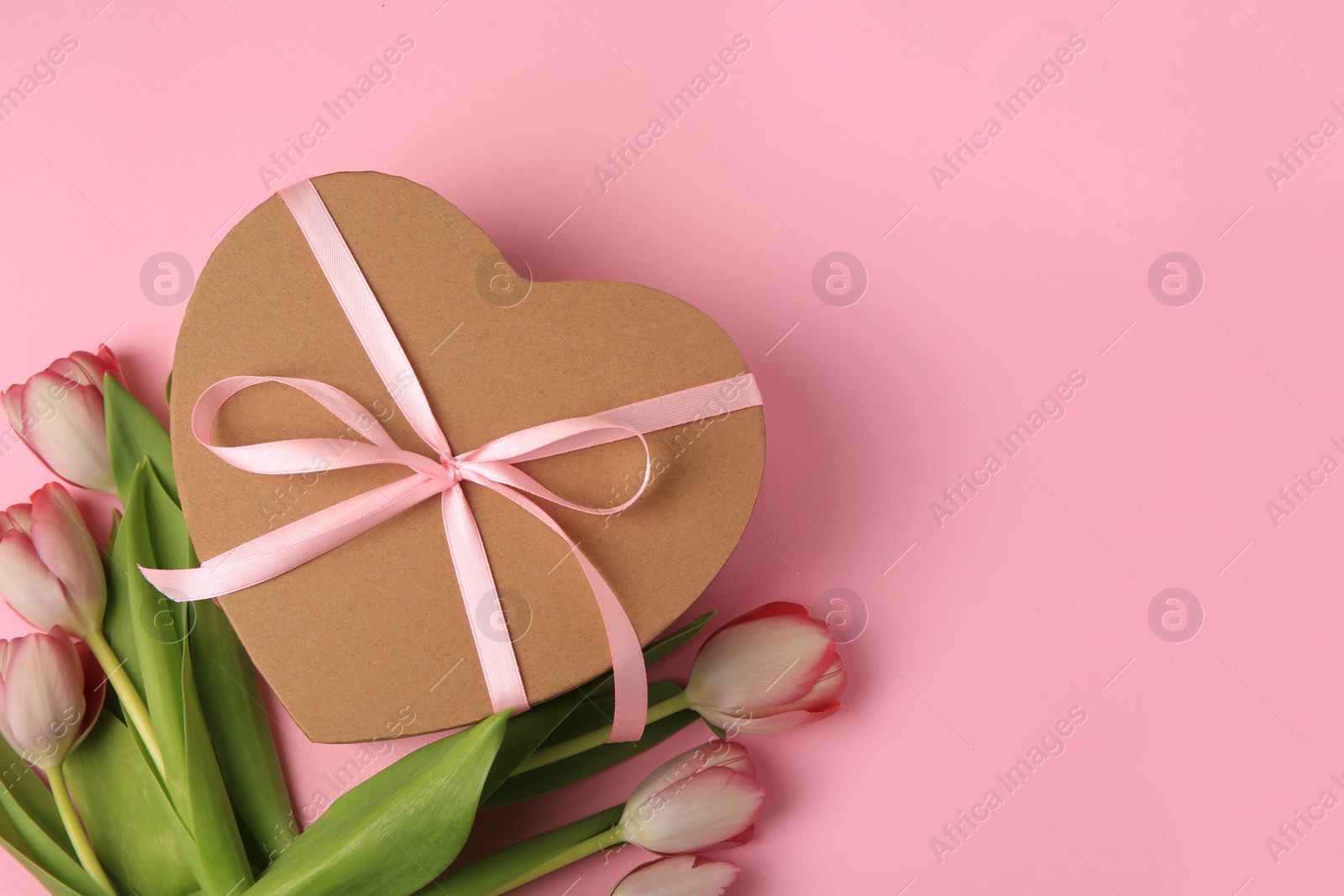 Photo of Heart shaped gift box with bow and beautiful tulips on pale pink background, flat lay. Space for text