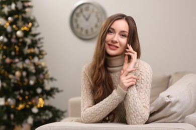 Beautiful young smiling woman near Christmas tree at home, space for text