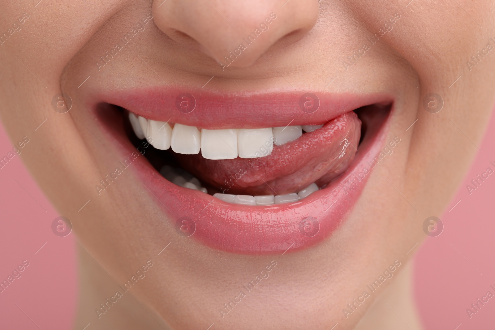 Photo of Young woman licking her teeth on pink background, closeup