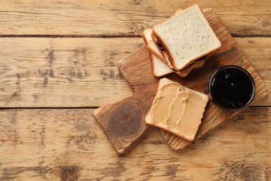 Photo of Tasty peanut butter sandwiches and jam on wooden table, top view. Space for text