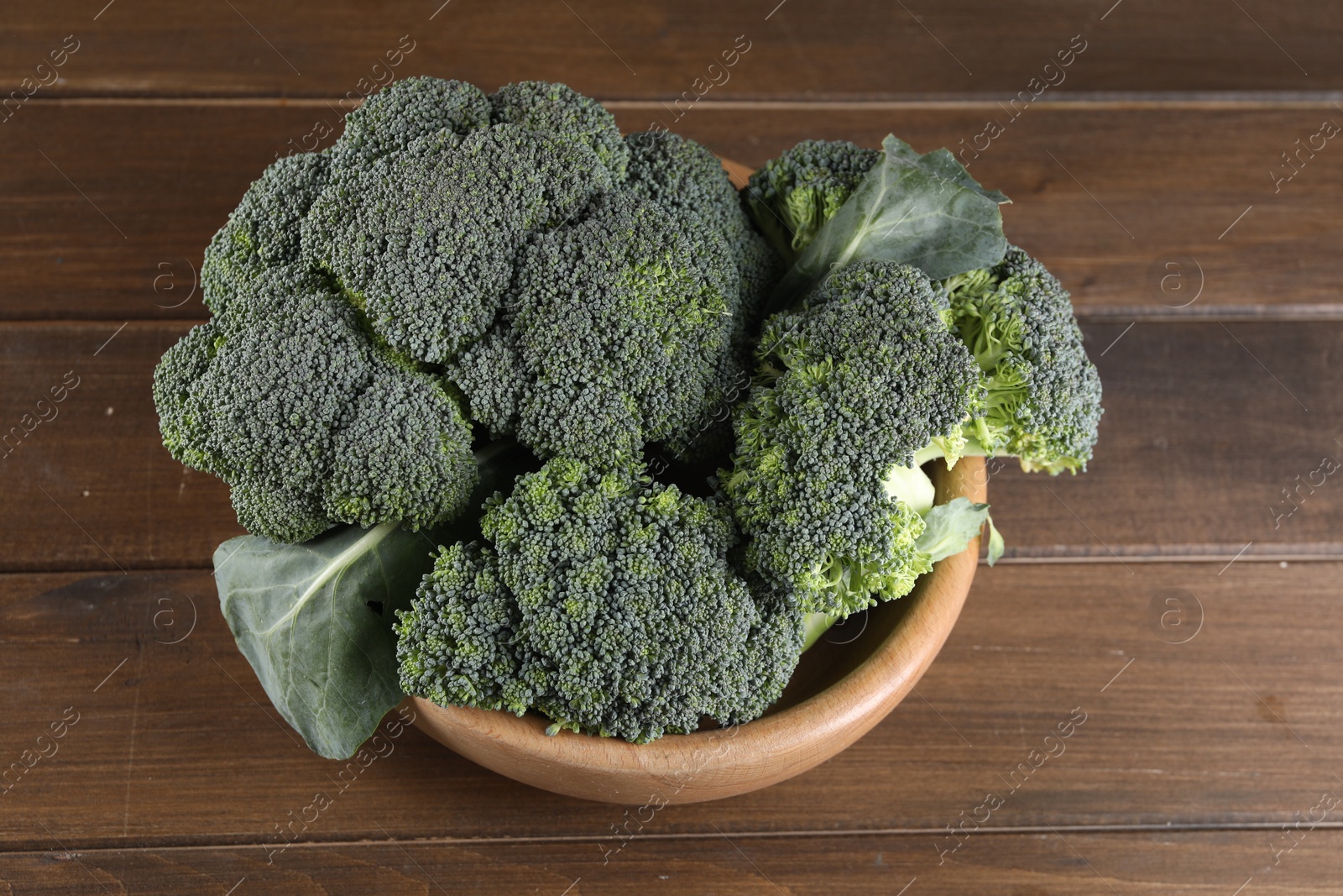 Photo of Bowl with fresh raw broccoli on wooden table, above view