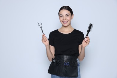 Portrait of happy hairdresser with professional scissors and vent brush on light background
