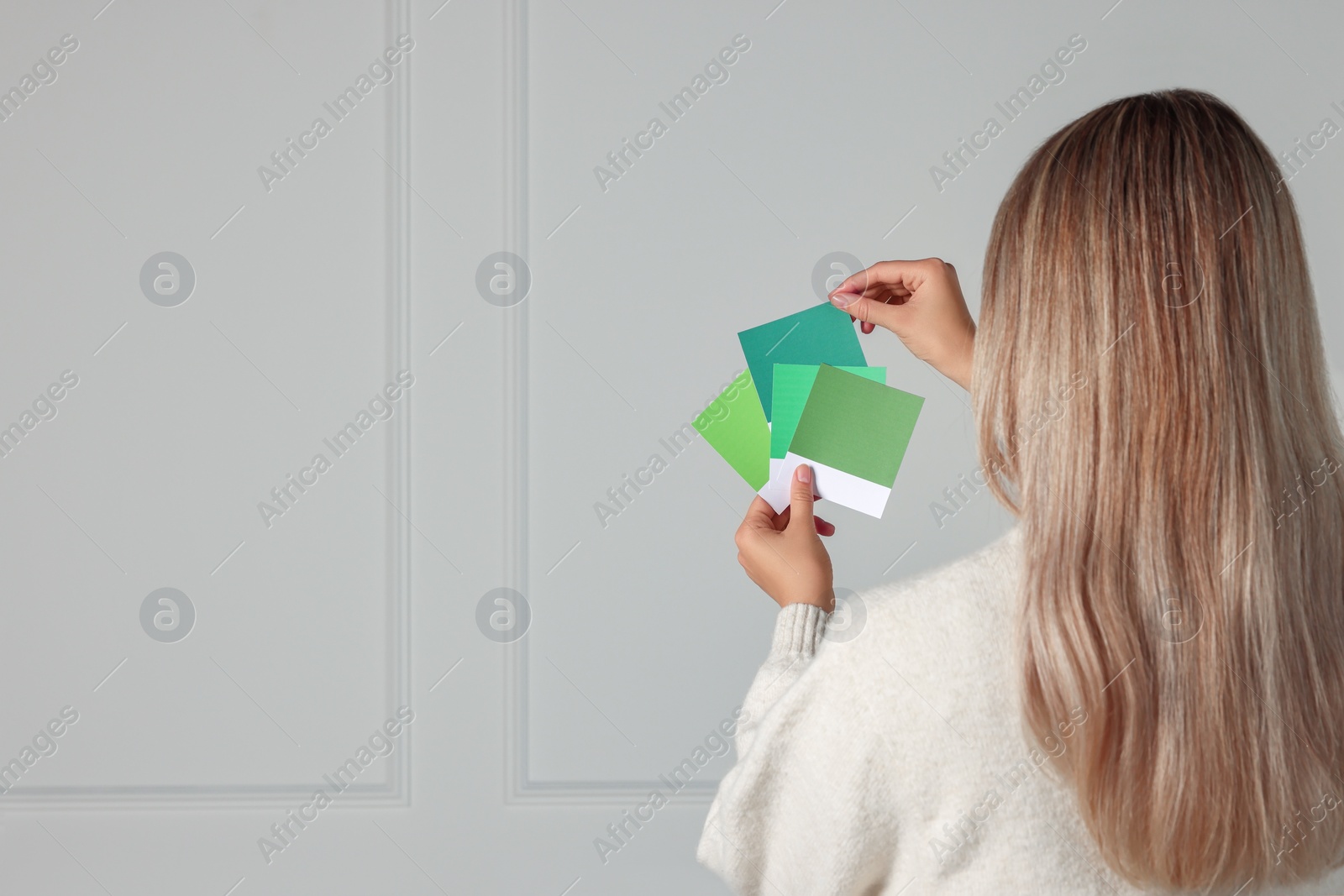 Photo of Woman with color sample cards choosing paint shade for wall indoors, back view. Interior design