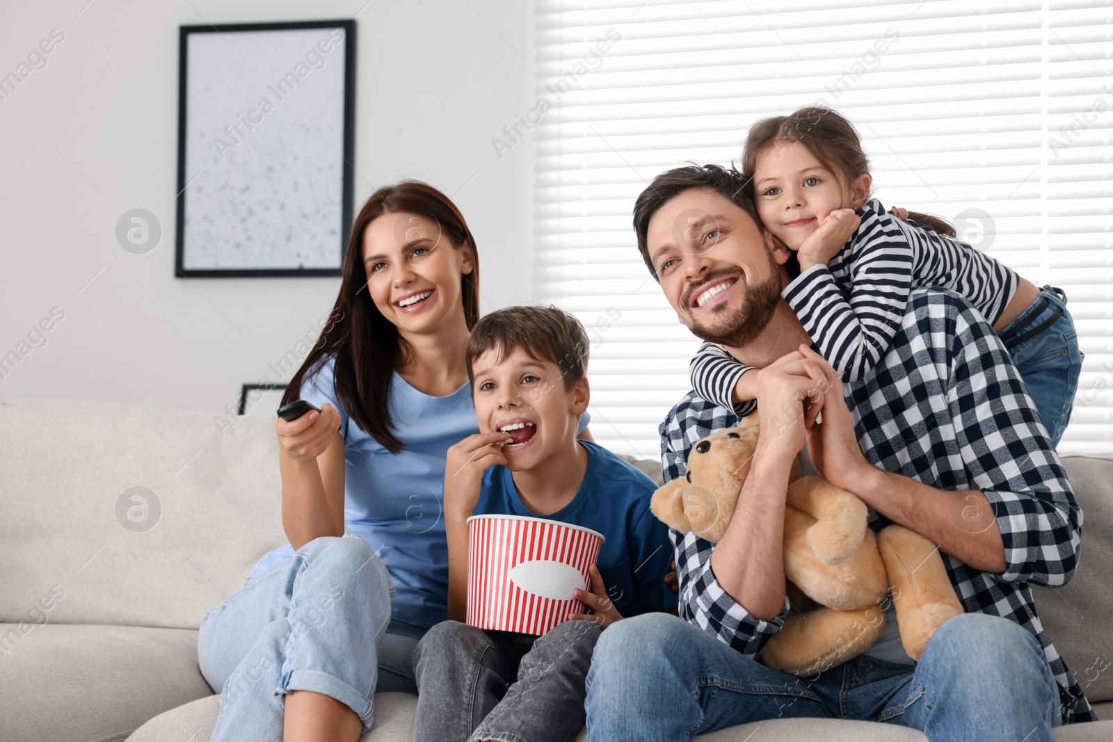 Photo of Happy family watching movie at home. Mother changing TV channels with remote control