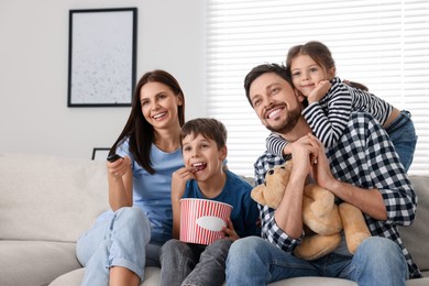 Photo of Happy family watching movie at home. Mother changing TV channels with remote control