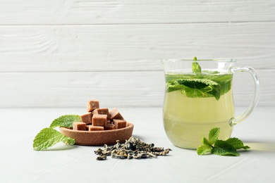 Photo of Cup with hot aromatic mint tea, dry leaves and sugar cubes on table