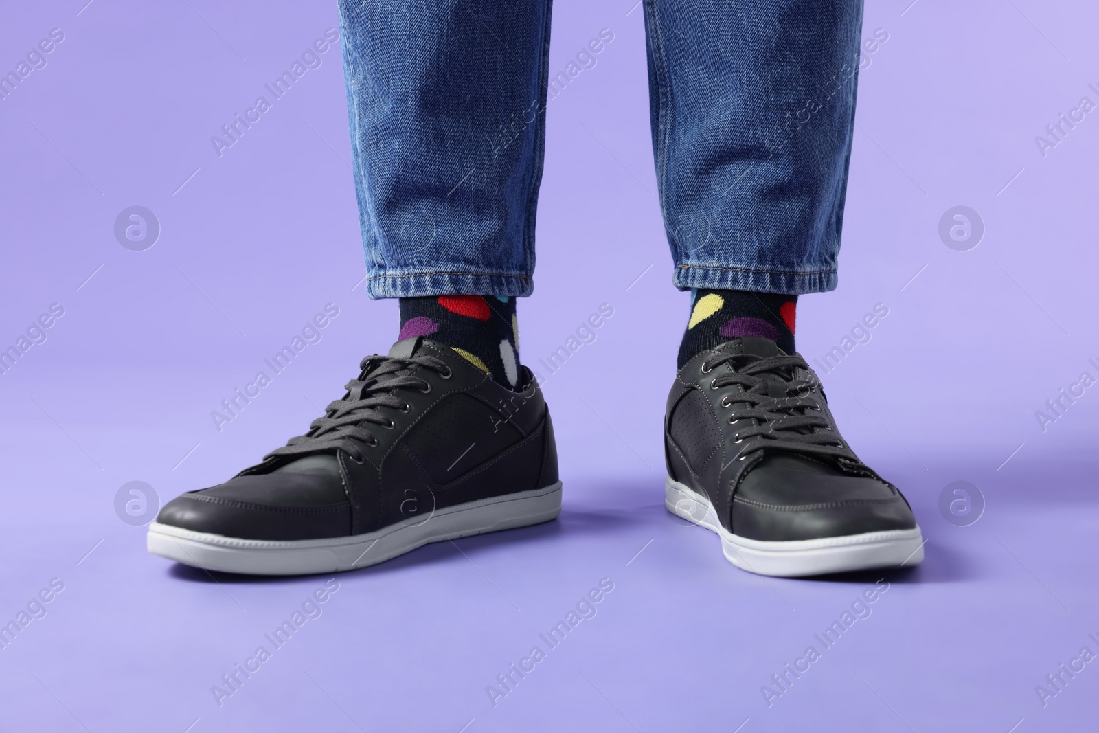 Photo of Man in stylish colorful socks, sneakers and jeans on violet background, closeup