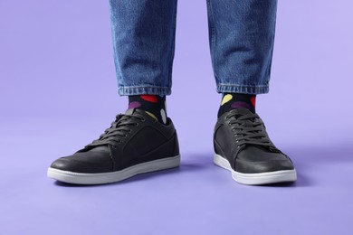 Photo of Man in stylish colorful socks, sneakers and jeans on violet background, closeup