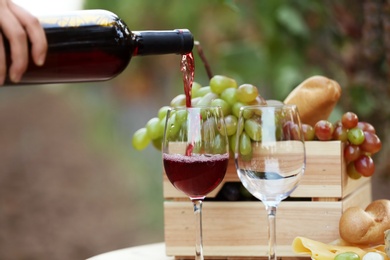 Woman pouring red wine into glass on table in vineyard