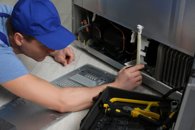 Male technician with screwdriver repairing refrigerator indoors