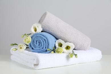 Photo of Clean soft towels with flowers on white table against light grey background