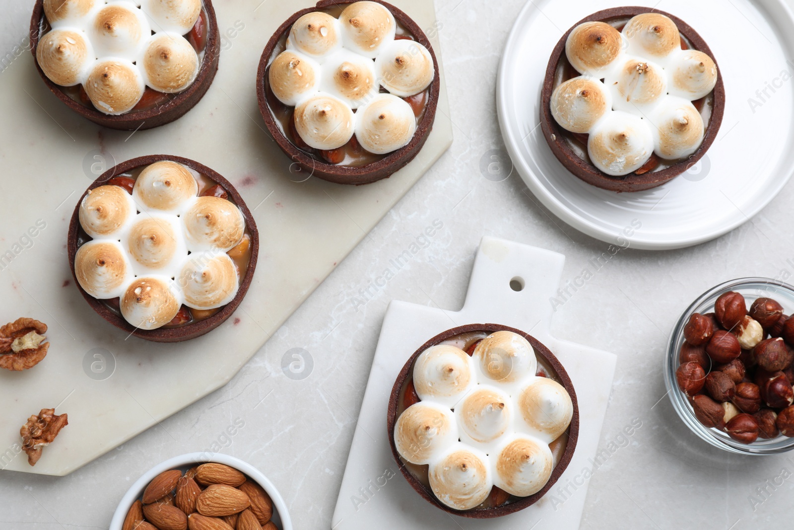 Photo of Delicious salted caramel meringue tarts and nuts on light grey marble table, flat lay