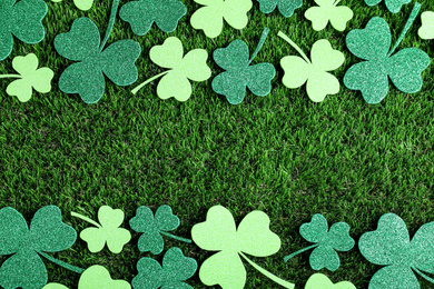 Photo of Frame made of clover leaves on green grass, flat lay with space for text. St. Patrick's Day celebration