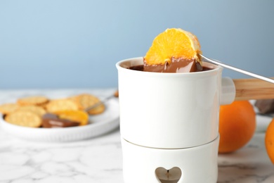 Photo of Dipping orange into fondue pot with chocolate on white marble table