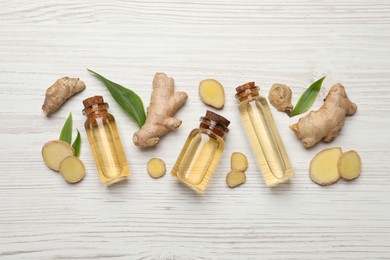 Photo of Glass bottles of essential oil and ginger root on white wooden table, flat lay