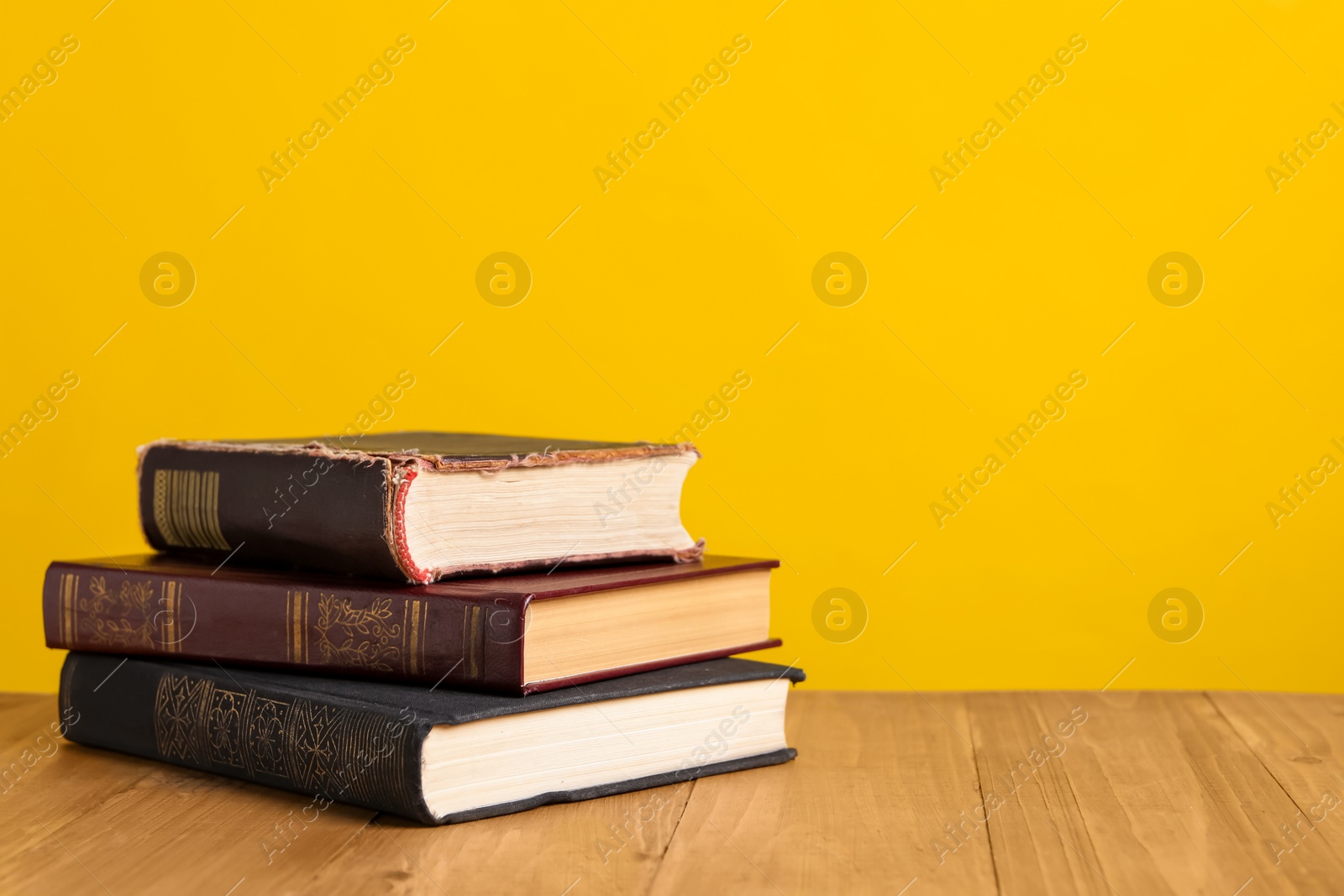 Photo of Stack of old hardcover books on wooden table against yellow background, space for text