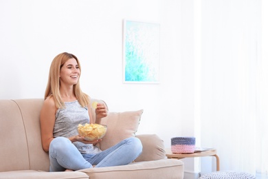 Woman with bowl of potato chips sitting on sofa in living room. Space for text