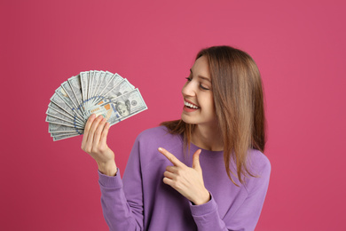 Happy young woman with cash money on pink background