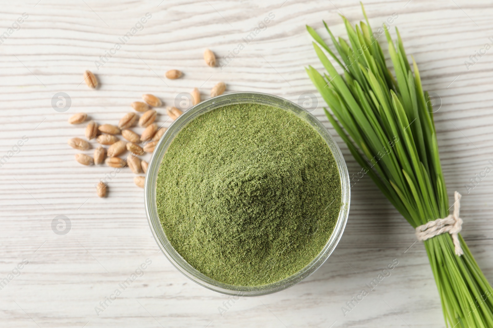 Photo of Wheat grass powder in bowl, seeds and fresh sprouts on white wooden table, flat lay