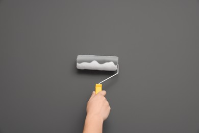 Photo of Worker using roller to paint wall with grey dye, closeup