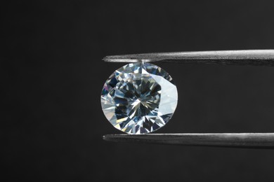 Tweezers with beautiful shiny diamond on black background, closeup