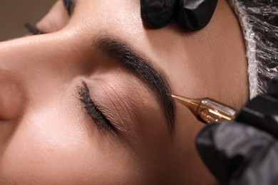 Photo of Young woman undergoing procedure of permanent eyebrow makeup in tattoo salon, closeup