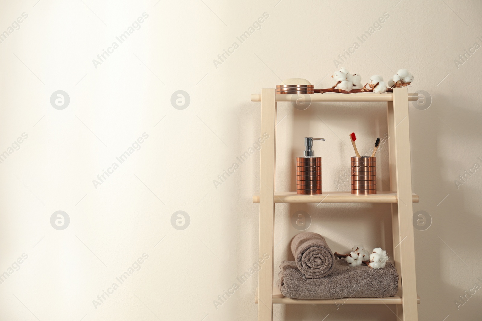 Photo of Wooden shelving unit with toiletries near beige wall indoors, space for text. Bathroom interior element