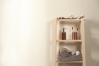 Photo of Wooden shelving unit with toiletries near beige wall indoors, space for text. Bathroom interior element