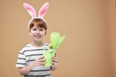 Photo of Easter celebration. Cute little boy with bunny ears and wrapped egg on dark beige background. Space for text