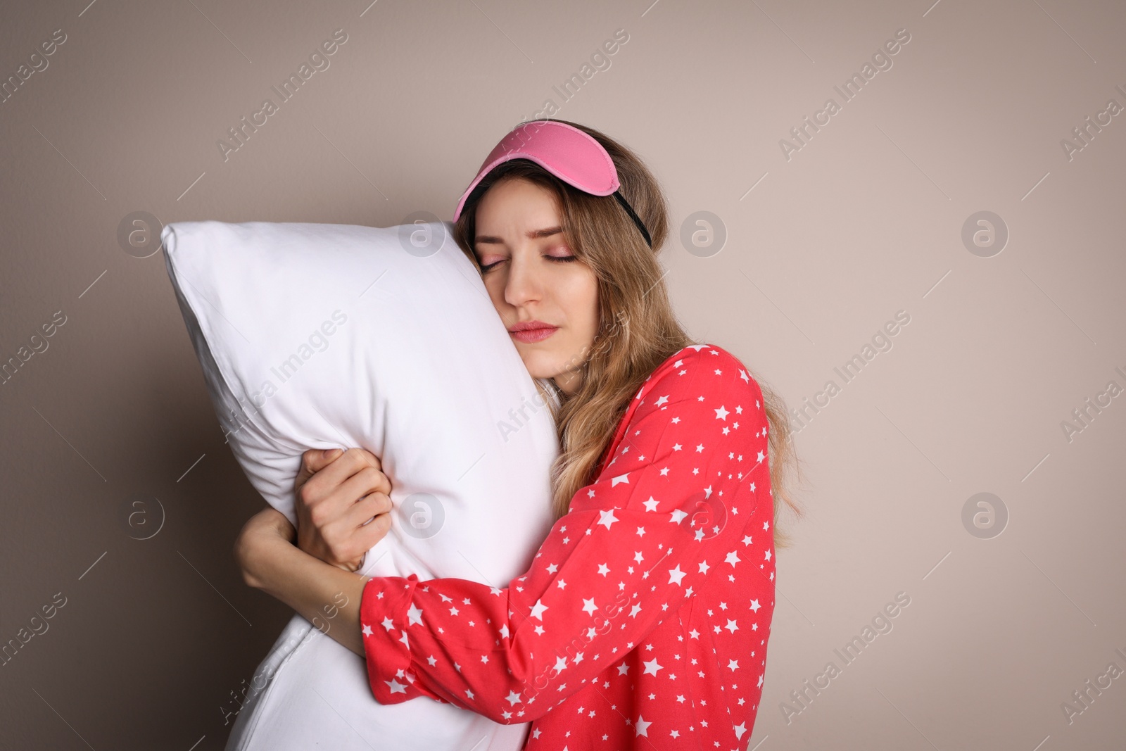 Photo of Young tired woman with sleeping mask and pillow on beige background