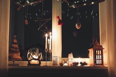 Burning candles and Christmas decor on window sill at night
