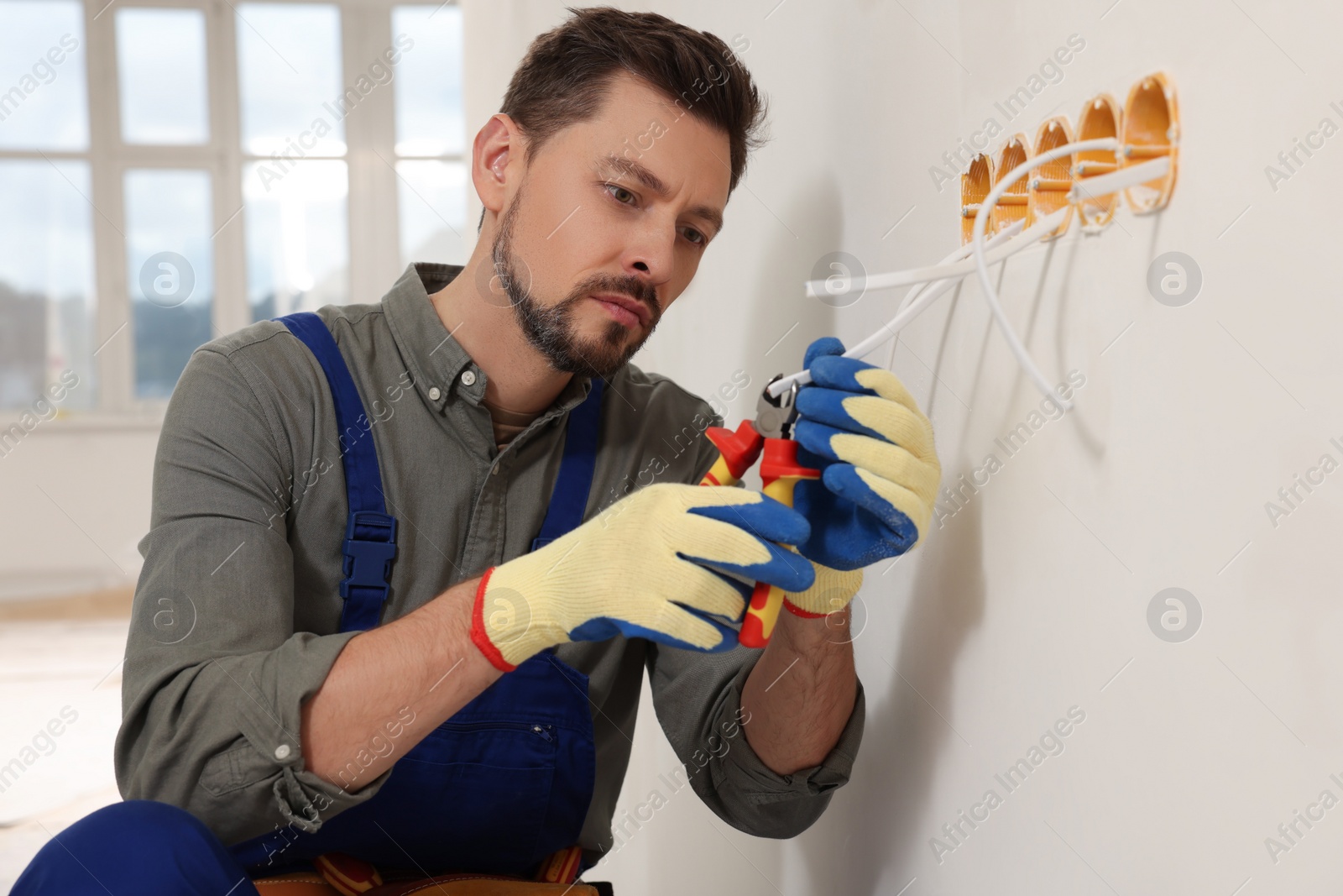 Photo of Electrician in uniform with pliers repairing power socket indoors