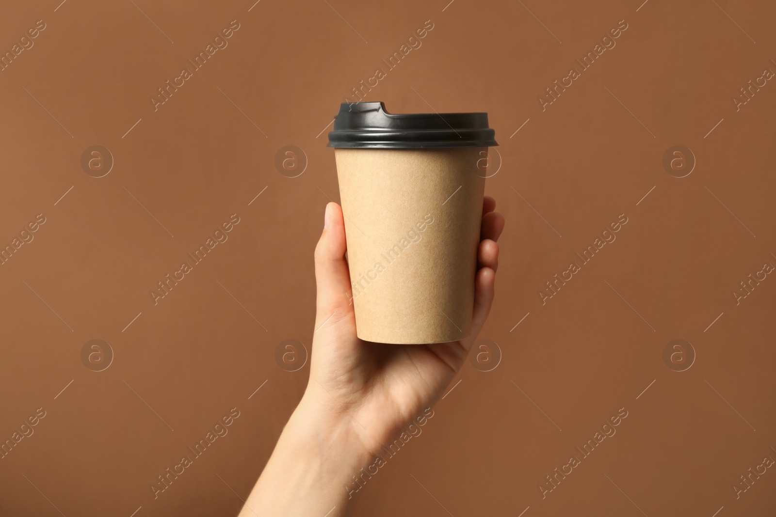 Photo of Woman holding takeaway paper coffee cup on brown background, closeup