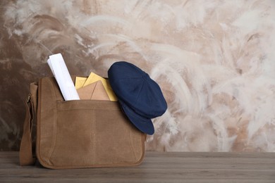 Postman's hat on bag full of letters and newspapers on wooden background. Space for text