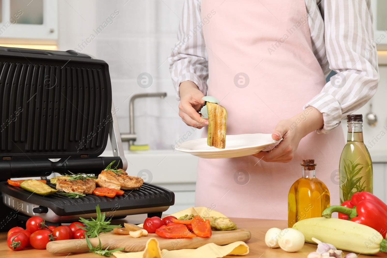 Photo of Woman cooking different products with electric grill at wooden table in kitchen, closeup