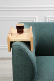 Photo of Glass of drink on sofa with wooden armrest table in room. Interior element