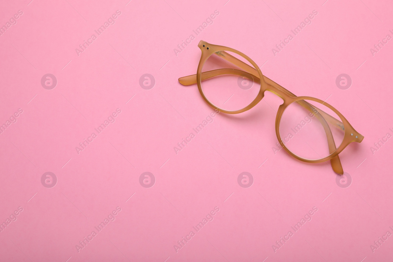 Photo of Glasses with corrective lenses on pink background, top view. Space for text