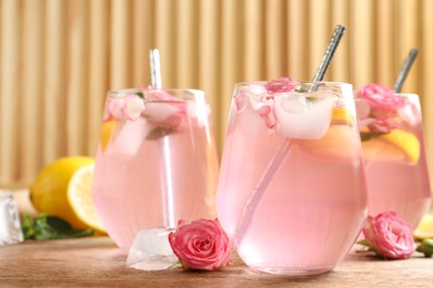 Photo of Delicious refreshing drink with rose flowers and lemon slices on wooden table, closeup