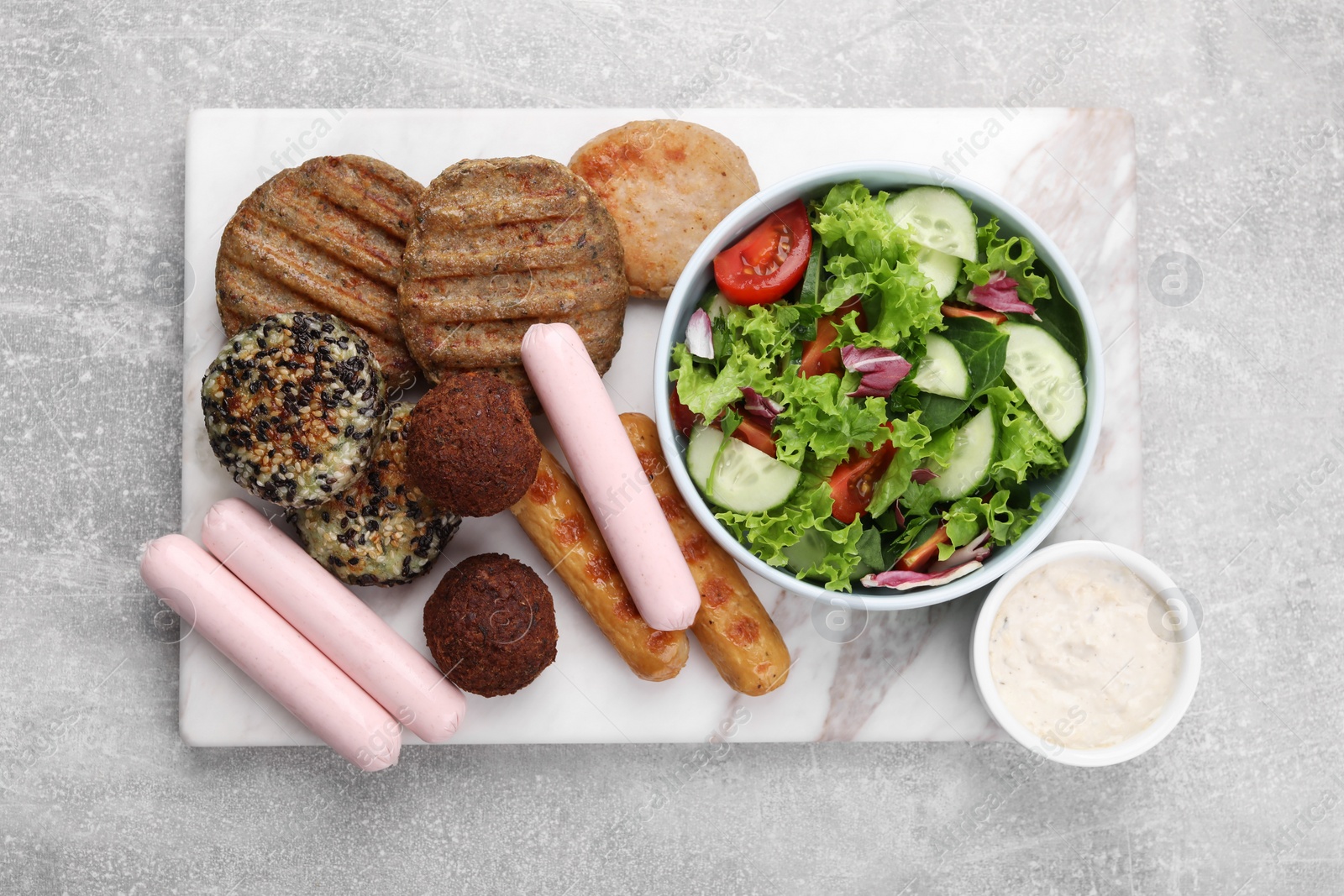 Photo of Different tasty vegan meat products, sauce and fresh vegetable salad on light grey table, top view