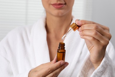 Woman with bottle of cosmetic serum and dropper on light background, closeup