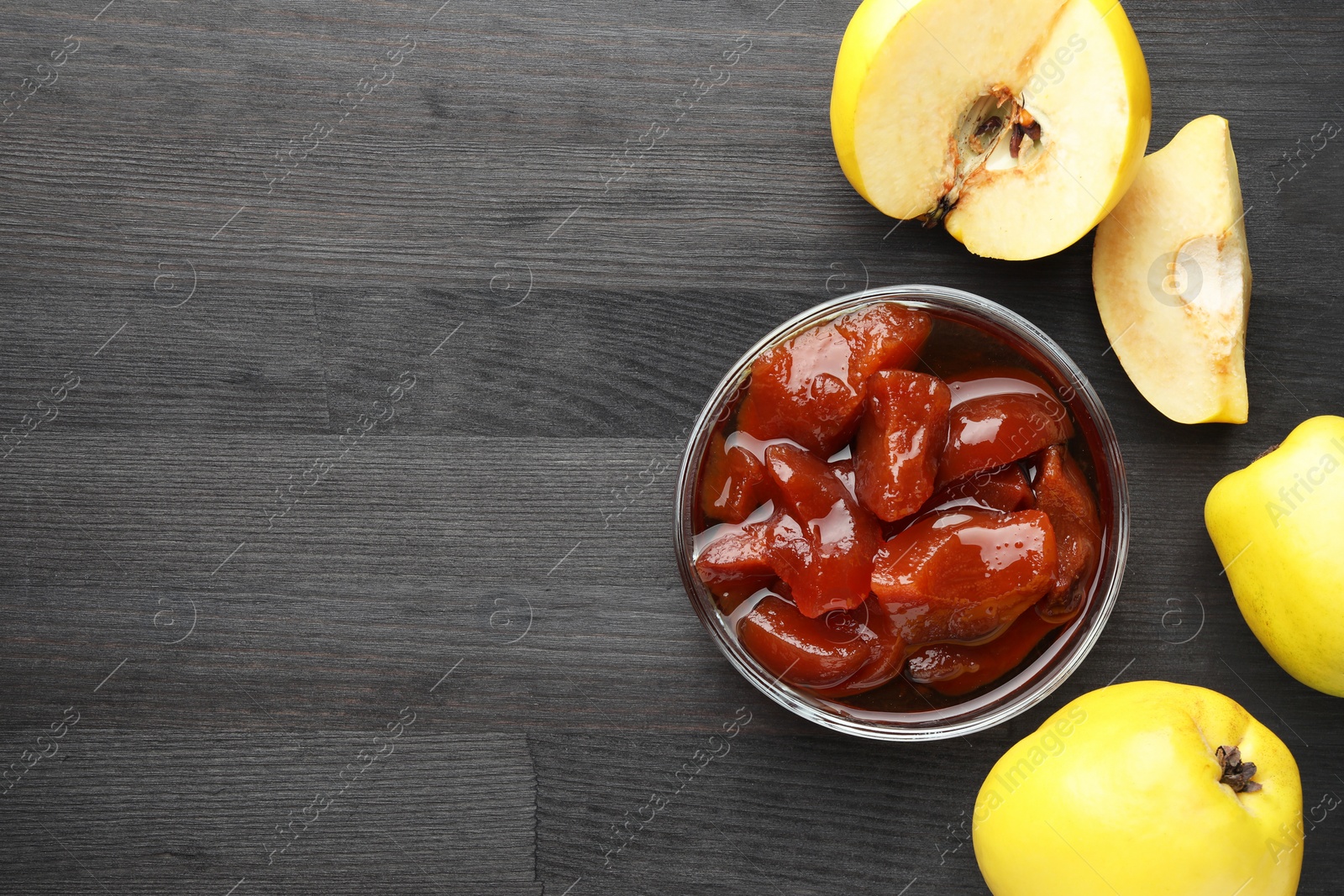 Photo of Quince jam in glass bowl and fresh raw fruits on grey wooden table, flat lay. Space for text