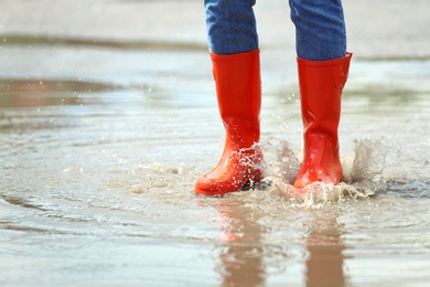 Woman with red rubber boots in puddle, closeup. Rainy weather