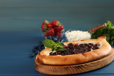 Photo of Delicious sweet cottage cheese pastry with cherry jam on blue wooden table, closeup. Space for text