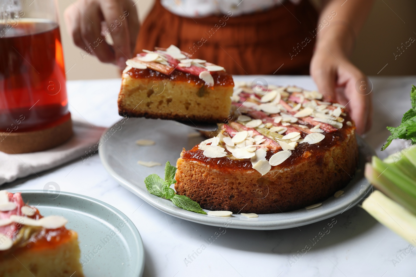 Photo of Woman taking piece of freshly baked rhubarb pie with almond flakes at white marble table, closeup