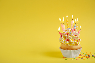 Photo of Birthday cupcake with burning candles on yellow background, space for text