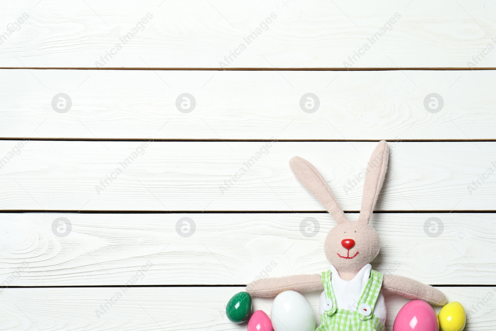 Photo of Flat lay composition of Easter bunny toy and colorful eggs on wooden background, space for text